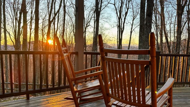 A wooden deck with two rocking chairs and a railing overlooking a forested area.