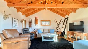 A cozy living room with leather chairs, a sofa, a TV, and rustic decor including a mounted deer head and skis.