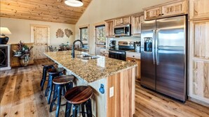 A kitchen with wooden cabinets, a stainless steel refrigerator, granite countertops, and bar stools. - Mountain Views/Fire Pit/Hot Tub/Game Room/Close 2 Strip (Sevierville)