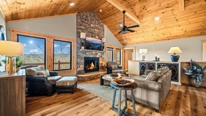 A spacious living room with a fireplace, wooden ceiling, and large windows offering a view of the outdoors. - Mountain Views/Fire Pit/Hot Tub/Game Room/Close 2 Strip (Sevierville)