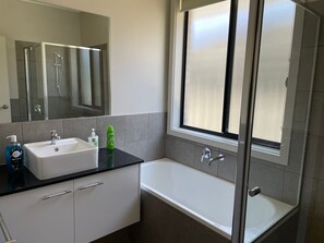 A modern bathroom with a large mirror, a white sink, a bathtub, and a window.