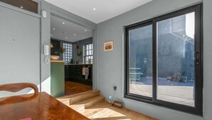 A modern interior with a wooden dining table, a kitchen area, and a large sliding glass door leading to an outdoor deck. - GuestReady - 2BR Flat with Private Roof Terrace (Edinburgh)