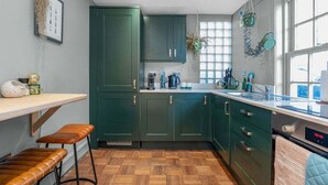 A kitchen with green cabinets, a wooden floor, a bar counter, and stools. - GuestReady - 2BR Flat with Private Roof Terrace (Edinburgh)