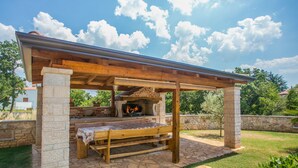 An outdoor patio with a stone floor, a wooden bench, and a stone fireplace under a pergola. - Villa Nevena by Interhome (Poreč)