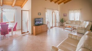 A spacious living room with a beige sofa, a TV on a wooden cabinet, and a dining area with red chairs. - Villa Nevena by Interhome (Poreč)