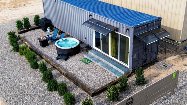 A compact, modern RV-style building with a blue roof, a hot tub, and a barbecue area.