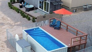 A swimming pool with a wooden deck, a hot tub, and a barbecue area.