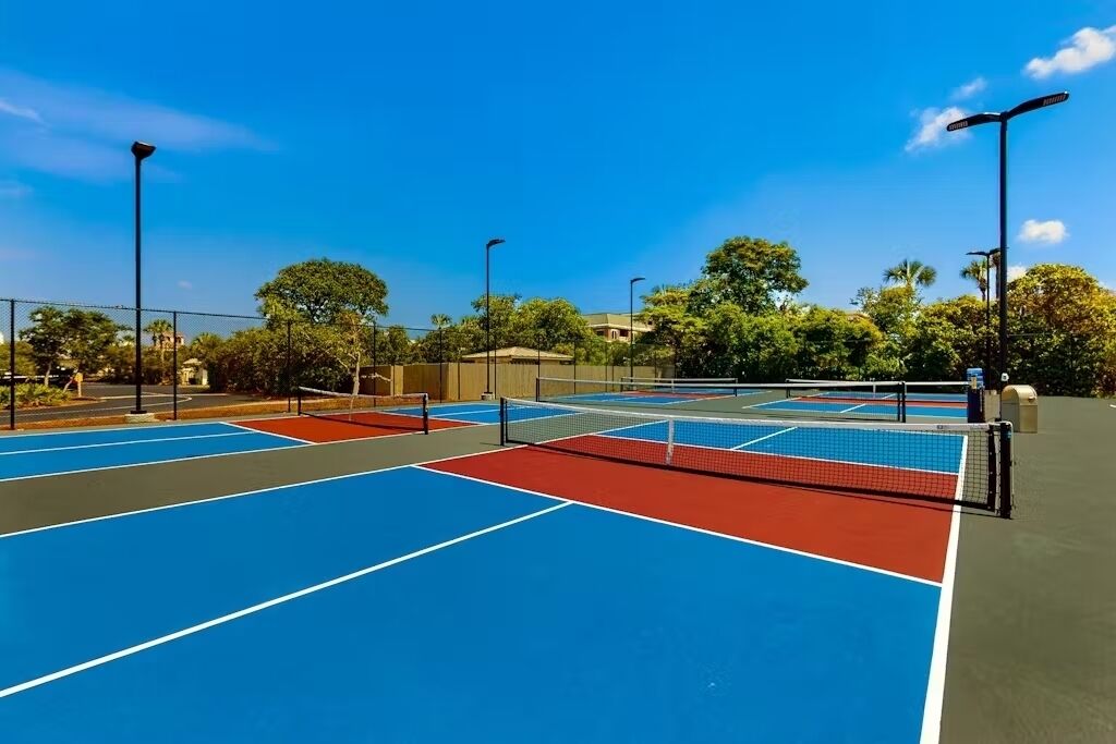 En udendørs tennisbane med flere baner, omgivet af træer og gadelamper.
