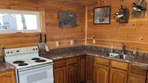 A kitchen with wooden cabinets, a white stove, granite countertops, and a window. - Lodge in Big Stone MN (Graceville)