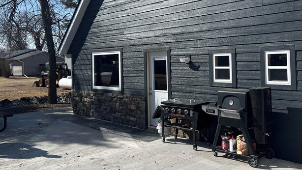 A two-story house with a stone foundation, a garage, and a backyard with a grill and a table. - Lodge in Big Stone MN (Graceville)
