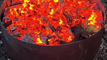 Metallinen nuotiopaikka, jossa hehkuvat hiilet ja palaa puu.