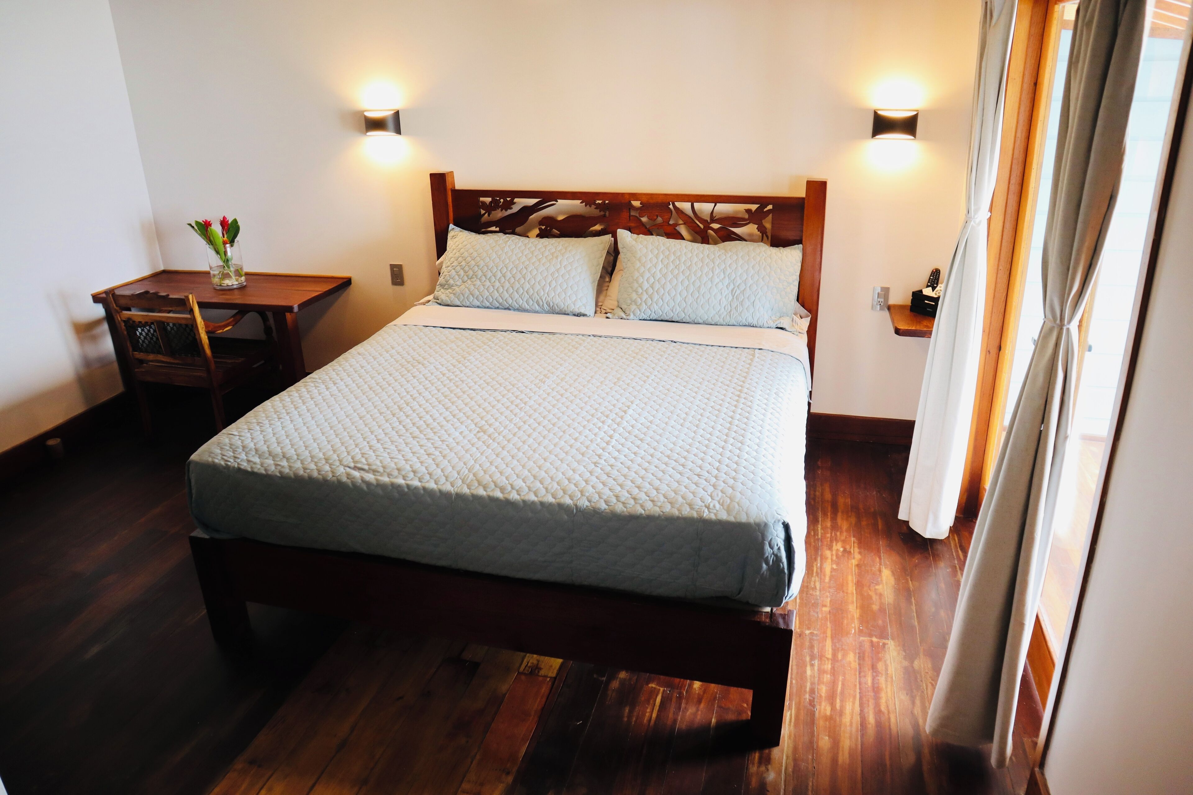 A neatly made bed with a quilted cover, a wooden headboard, and two wall-mounted light fixtures.