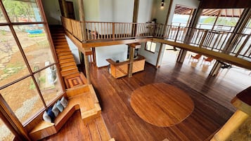 Un interior espacioso con suelo de madera, una zona de estar central y una escalera que conduce a un nivel superior.