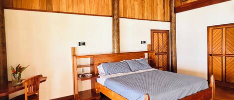 Ein Schlafzimmer mit Holzrahmen, das ein Bett, einen Nachttisch, einen Sessel und einen Schreibtisch beinhaltet.