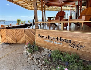 A wooden sign for Bocas Beachfront Lodge on Carenero Island, featuring a view of the ocean and outdoor seating area. - Bocas Beachfront Lodge (Bocas del Toro)
