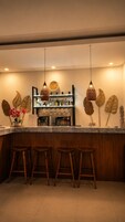 Una zona de bar con mostrador de mármol, taburetes de madera, decoración mural y lámparas colgantes.