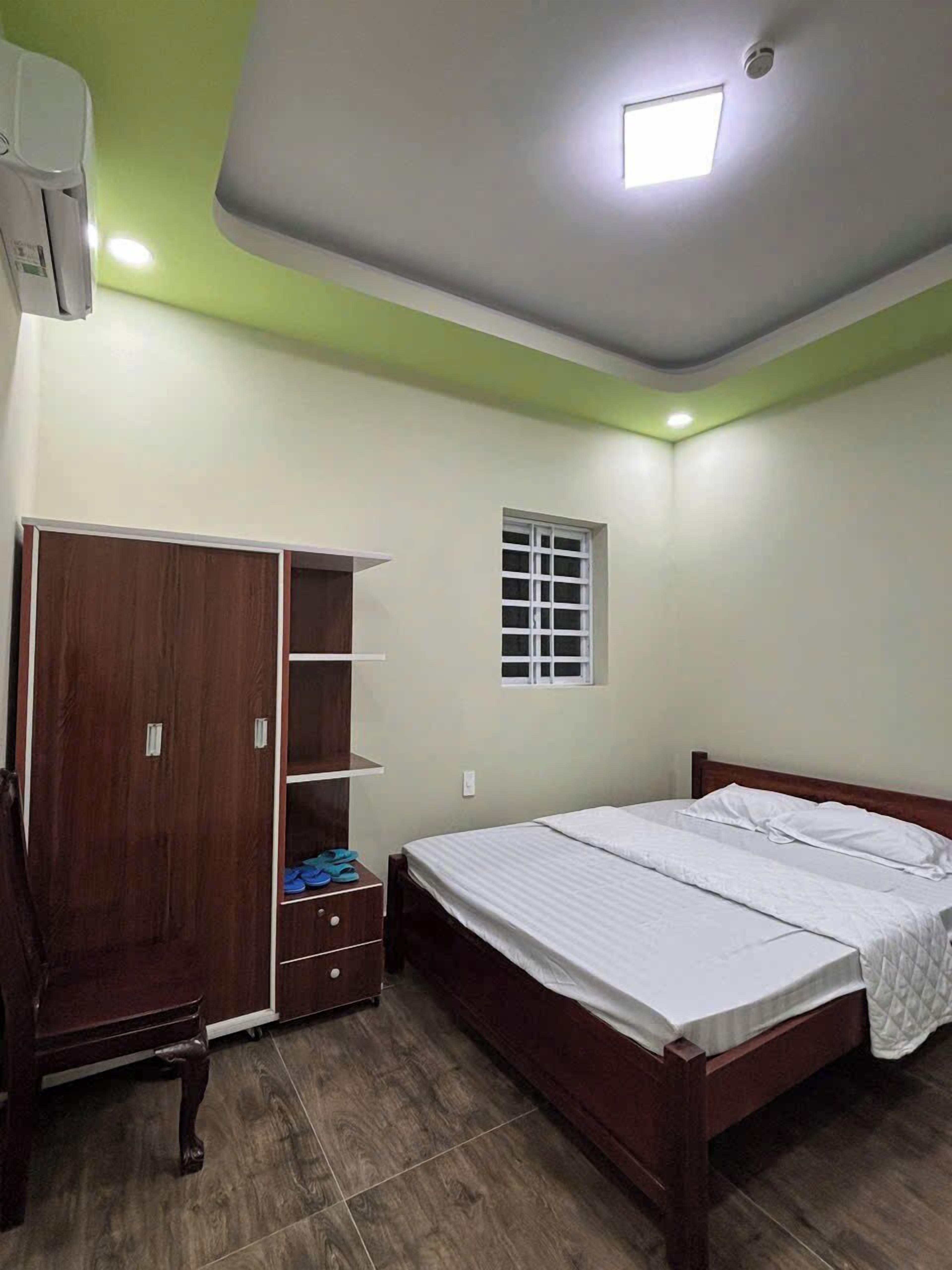 Un dormitorio con cama de madera, armario con estantes, una ventana pequeña y una lámpara en el techo.