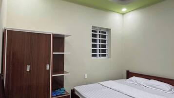 Un dormitorio con cama de madera, armario con estantes, una ventana pequeña y una lámpara en el techo.