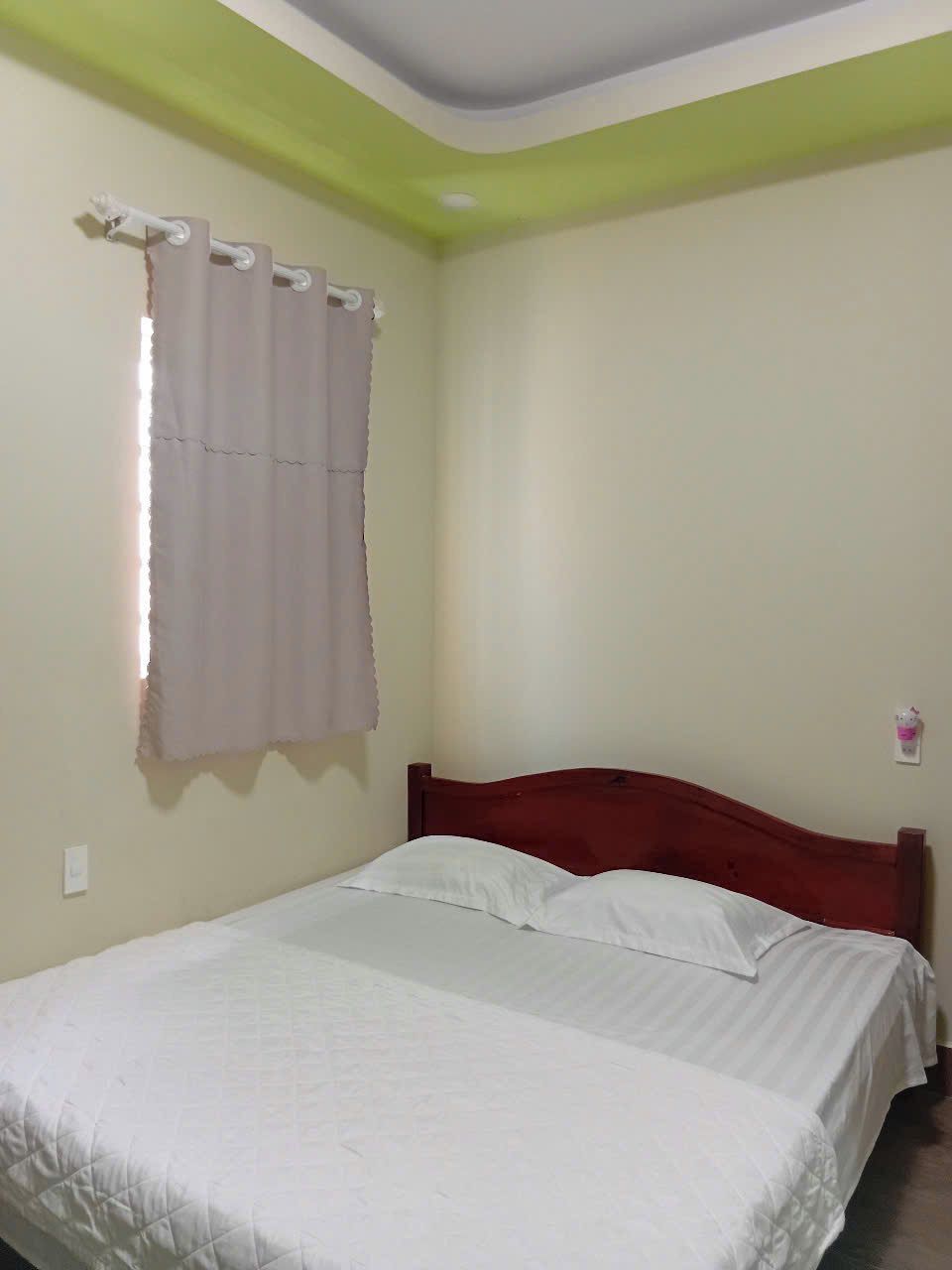 Een enkel bed met houten hoofdeinde in een kamer met effen muren en een groen plafond.