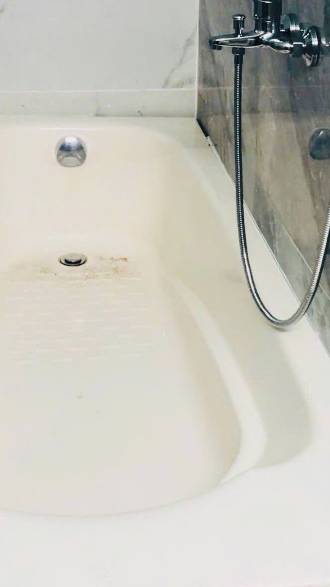 Una bañera con manguera de ducha, desagüe y pared de mármol.