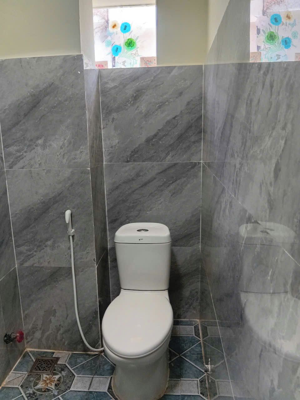 A bathroom with a toilet, a shower, and a window with a floral design.