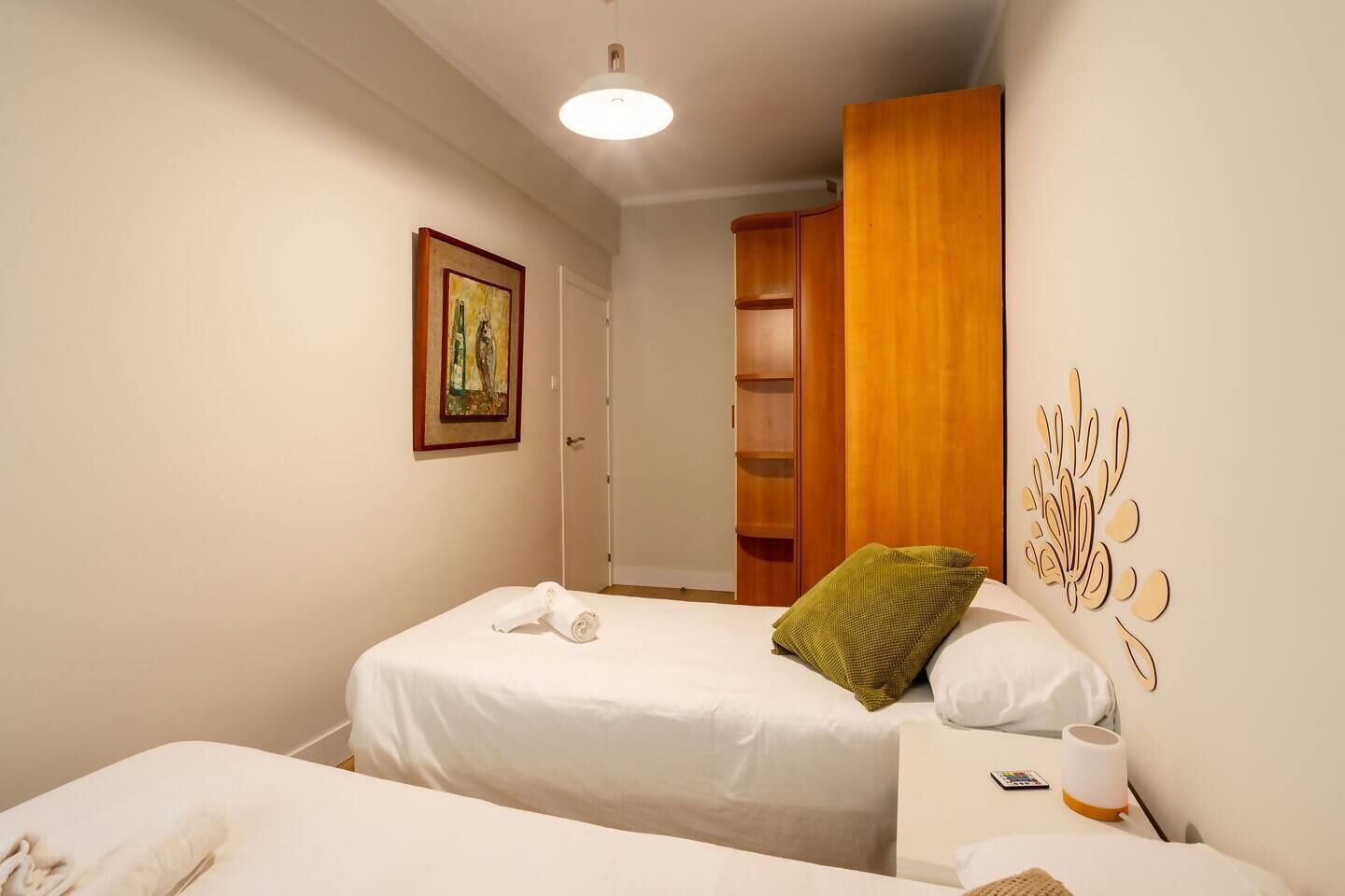 A hotel room with two beds, a wooden wardrobe, a painting on the wall, and a decorative wall piece.