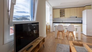 Una cocina moderna con armarios de madera, un comedor con sillas blancas y un televisor sobre un mueble de madera.