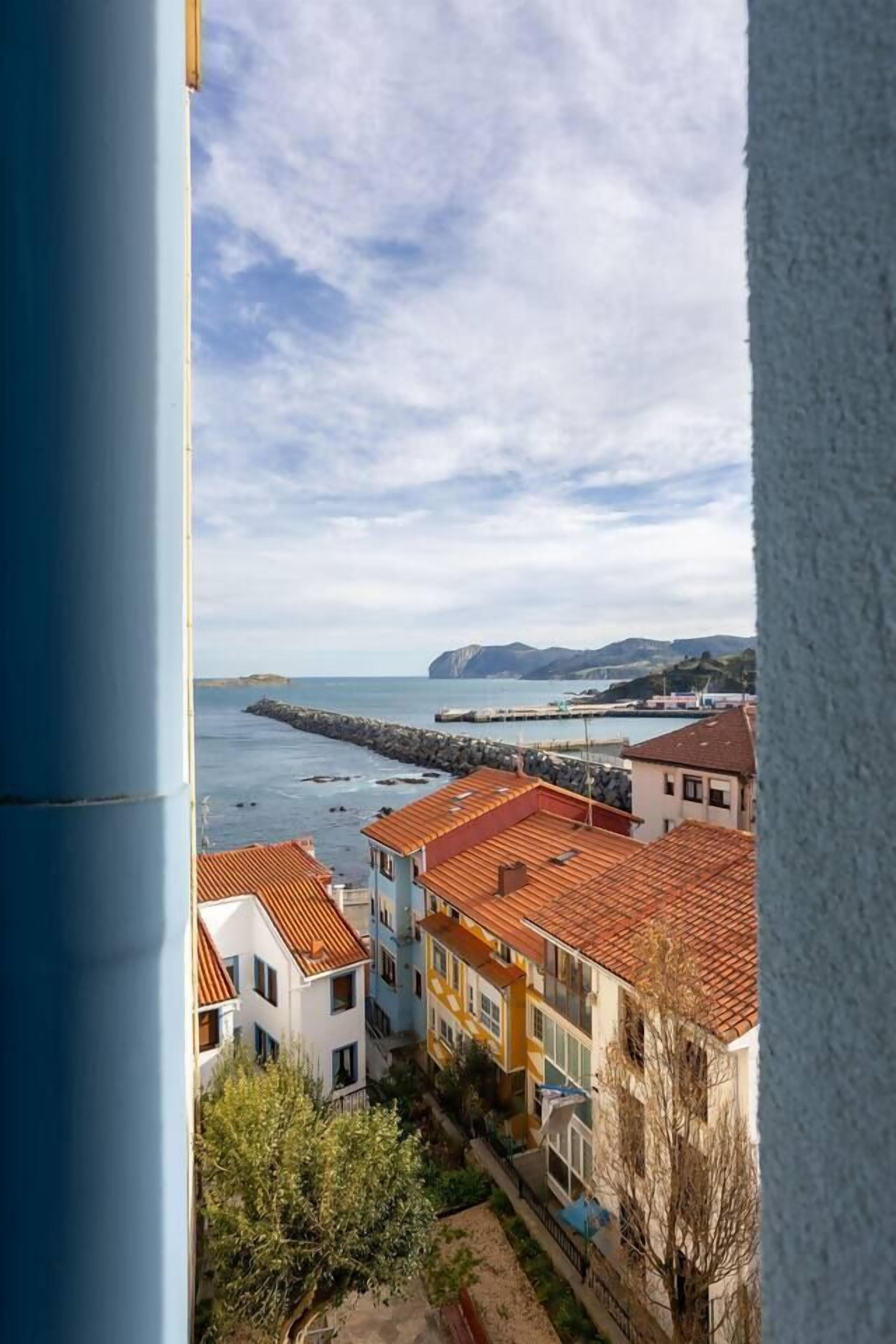 Un quartier résidentiel en bord de mer, avec des maisons à étages, une digue rocheuse et une vue dégagée sur la mer.