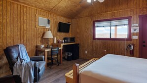 A room with a bed, a desk with a computer, a chair, and a ceiling fan.