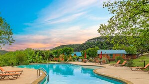 A swimming pool with a 3ft depth marker, surrounded by lounge chairs and a wooden cabin.