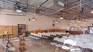 A spacious hall with rows of white chairs, a wooden bookshelf, and ceiling fans.