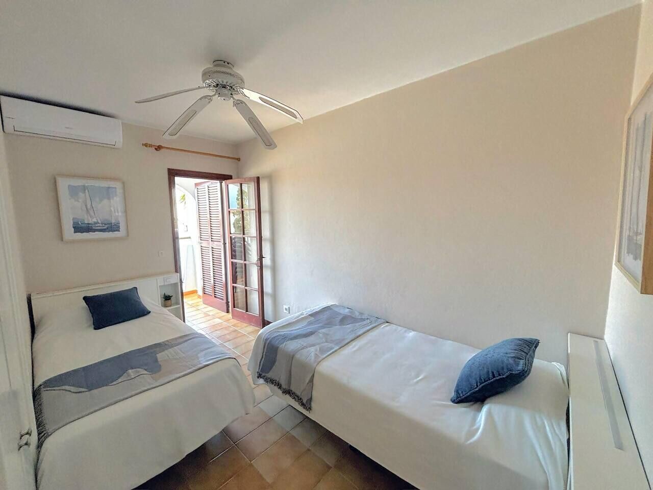 Habitación con dos camas individuales, ventilador de techo, aire acondicionado y puerta que da a un espacio exterior.