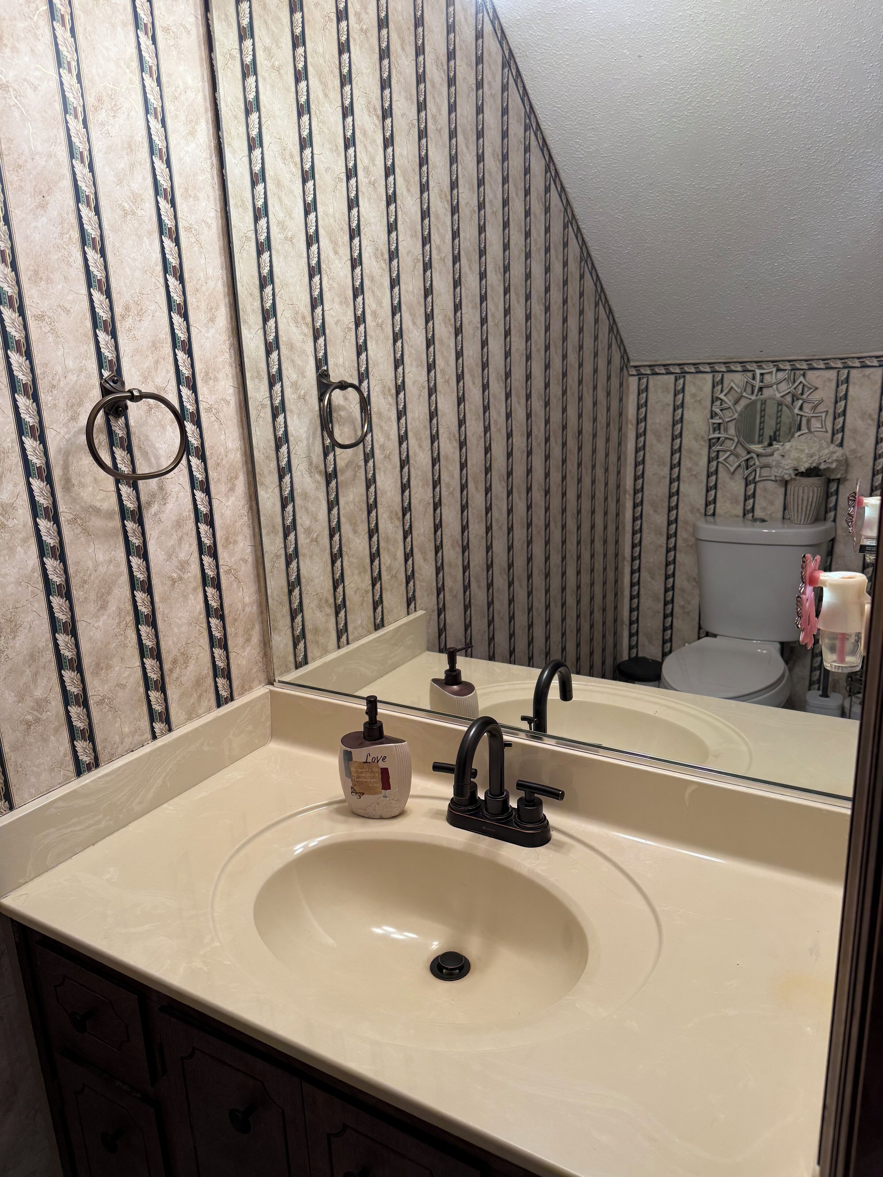 Une salle de bain avec un lavabo beige, un robinet noir et un papier peint à rayures.