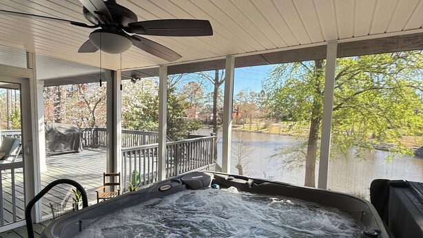 A hot tub with a ceiling fan, surrounded by a covered deck with a view of a lake and trees. - Masters week with Hot Tub (Martinez)