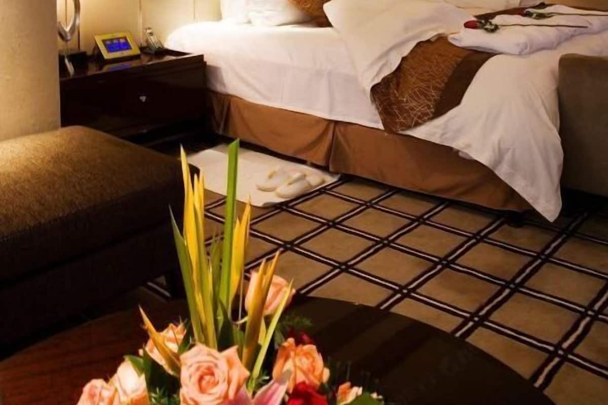 Ein Hotelzimmer mit einem großen Bett, Nachttischen, einem Beistelltisch, einem Sessel und einem kleinen Tisch mit Blumen.
