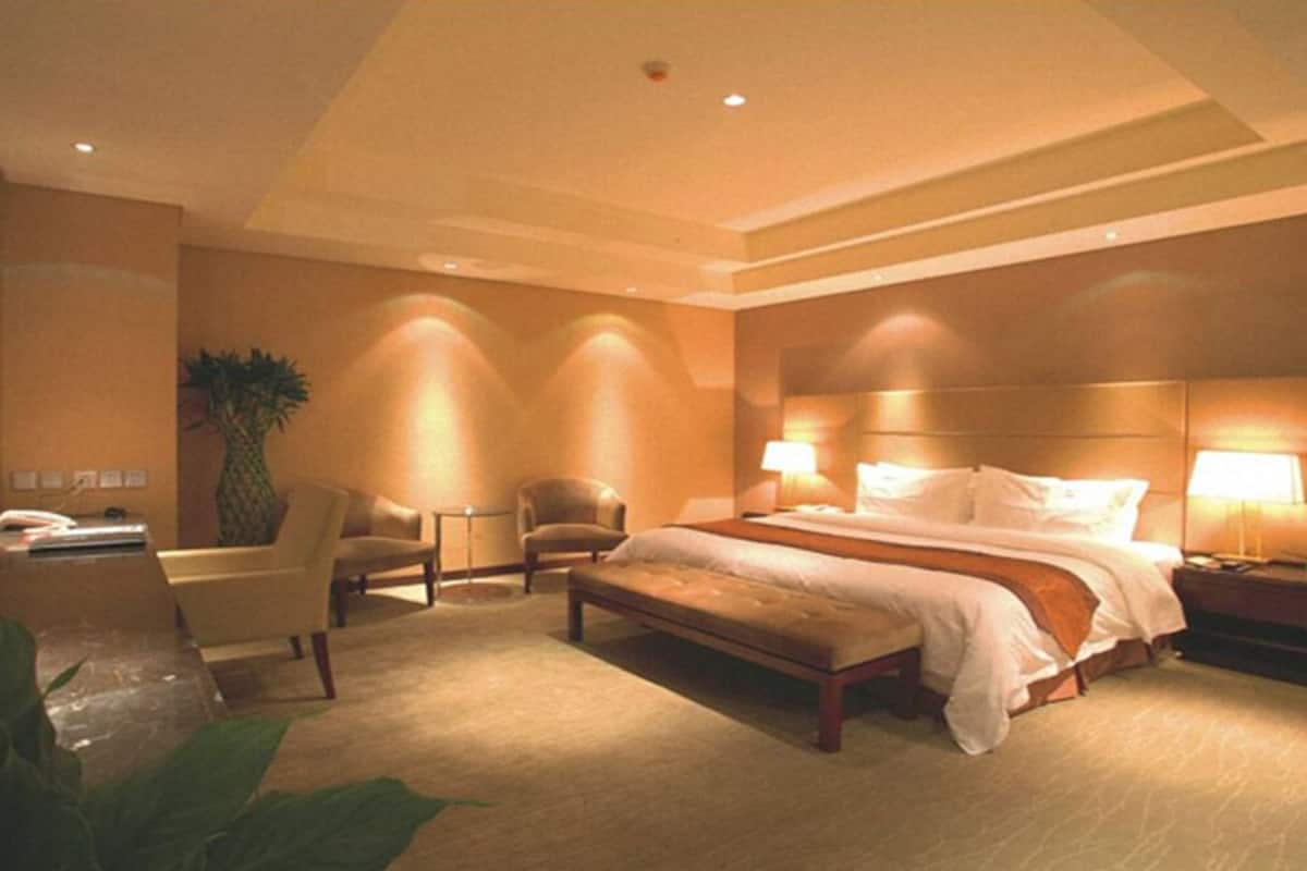 Ein Hotelzimmer mit einem großen Bett, zwei Nachttischen mit Lampen, einem Sessel und einem kleinen Tisch mit einer Pflanze.