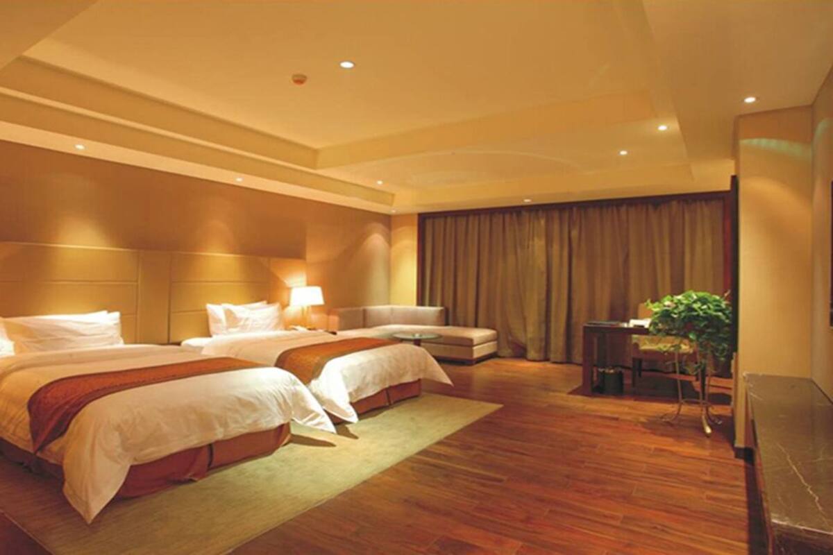 Ein Hotelzimmer mit zwei Betten, einem Sofa, einem Schreibtisch und einer Pflanze.