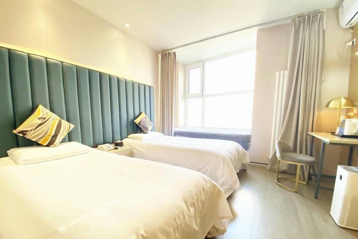 Ein Hotelzimmer mit zwei Betten, einem Schreibtisch, einem Stuhl und einem Fenster mit Vorhängen.