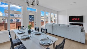 A modern living room with a grey sofa, a dining table set with plates and glasses, and a TV mounted on the wall displaying 'NETFLIX'. - Luxury 3BDR large House-4 mins to Seton Hospital-Parking / Pet Free  (Calgary)