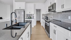 A modern kitchen with white cabinets, stainless steel appliances, and a black granite countertop. - Luxury 3BDR large House-4 mins to Seton Hospital-Parking / Pet Free  (Calgary)