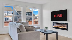 A modern living room with a grey sofa, a flat-screen TV mounted on the wall, and a fireplace. - Luxury 3BDR large House-4 mins to Seton Hospital-Parking / Pet Free  (Calgary)