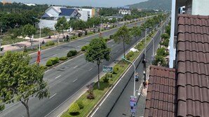 A multi-story building with a balcony, a road with trees and a clear sky. - Kim Ngan Motel (Chau Doc)