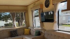 Un interior de caravana acogedor con un sofá, una mesa redonda y un televisor montado en la pared.