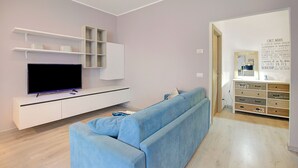 A modern living room with a flat-screen TV, a light blue sofa, white shelving, and a wooden cabinet.