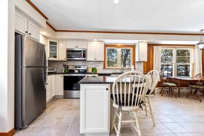 A modern kitchen with white cabinets, stainless steel appliances, and a dining area with wooden chairs. - Beachfront, Just steps and you're on the beach! (Saco)