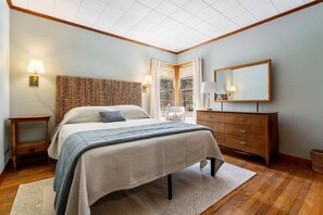 A bedroom with a large bed, a wooden headboard, a nightstand, a dresser, and a mirror.