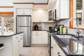 A modern kitchen with white cabinets, a stainless steel refrigerator, a granite countertop, and a sink with a modern faucet.
