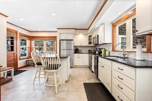 A modern kitchen with white cabinets, a stainless steel refrigerator, and a dining area with a wooden table and chairs.