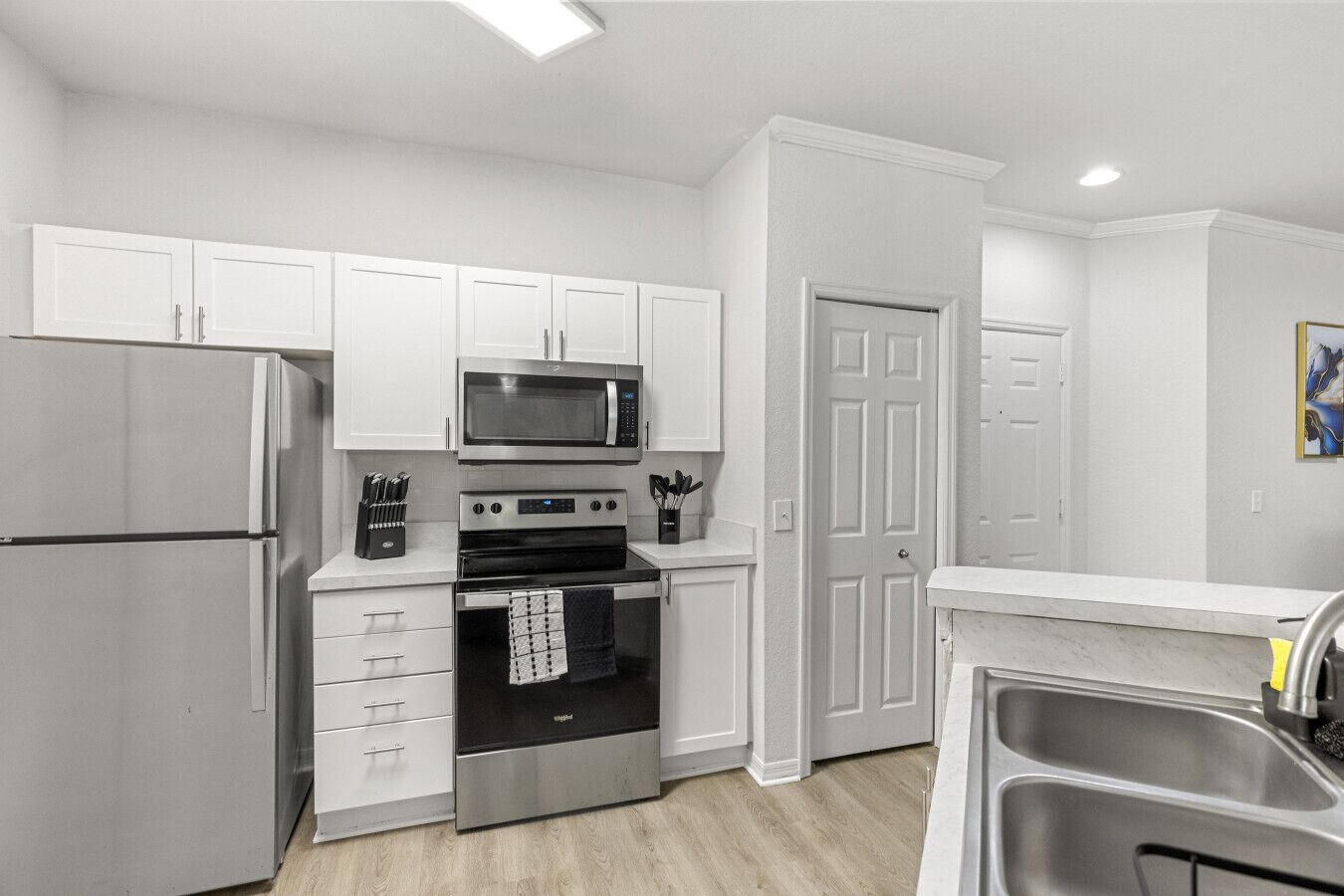 A modern kitchen with white cabinets, stainless steel appliances, and a wooden floor.