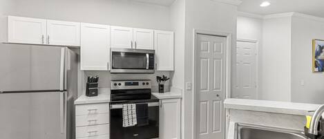 A modern kitchen with white cabinets, stainless steel appliances, and a wooden floor.